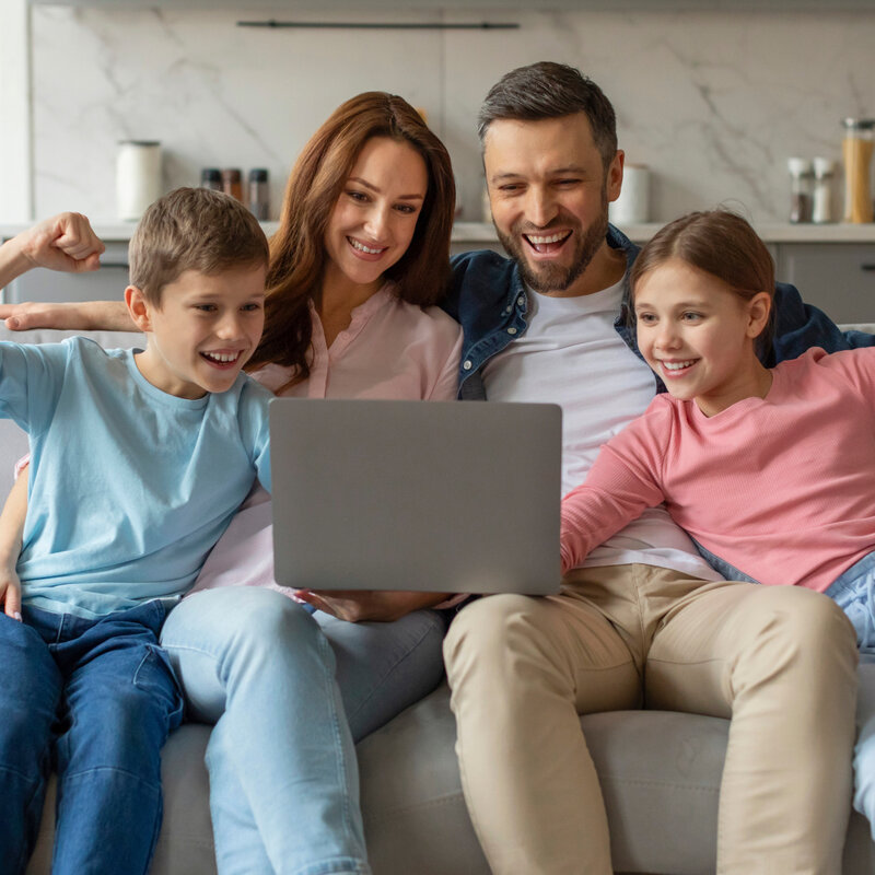 Happy family with two children sitting on a couch and celebrating as they look at a laptop screen at home